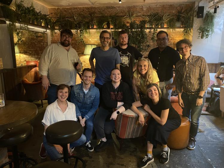 A group of smiling people pose inside a café in London with plants in the background.