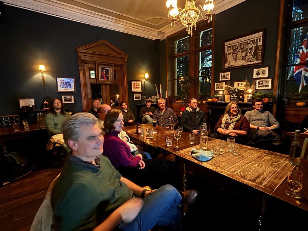 Members of the group sit around a table at the Leather Exchange pub and listen to the results of the 2025 story contest.