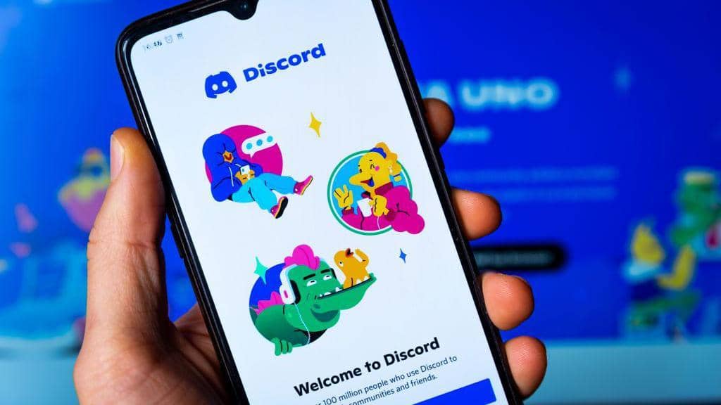 A person holds up a smartphone with the splash page of the Discord app on it.